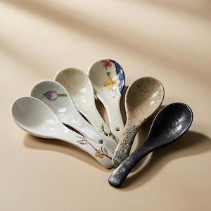 May include: Six ceramic spoons with diverse patterns and colours. The spoons are white, beige, and black, with floral, speckled, and textured designs. Each spoon has a small hole in the handle. The spoons are suitable for serving food.