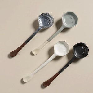 Puede incluir: Vista superior de cuatro cucharas de servir. Las cucharas son plateadas, grises, blancas y negras. Cada cuchara tiene un diseño de mango único, algunas con un acento de madera. Las cucharas están dispuestas sobre un fondo neutro.