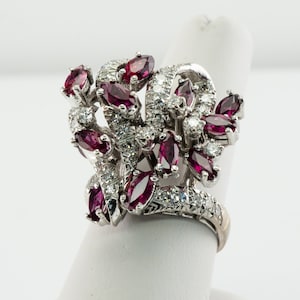 May include: A silver ring with a cluster of red ruby and white diamond stones set in a floral design.