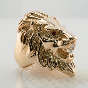 Op de afbeelding: Een gouden ring met een leeuwenkop, met een rode edelsteen als oog en heldere edelstenen in de bek.