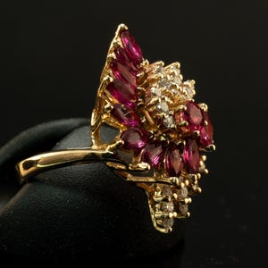 May include: A gold ring with a cluster of marquise-cut ruby gemstones and small diamonds. The ring has a floral design, with the rubies forming the petals and the diamonds the center.