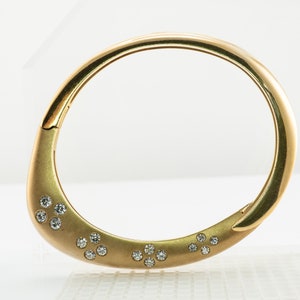 May include: A gold bangle bracelet with a smooth, rounded surface and a row of small, clear diamonds set into the metal.
