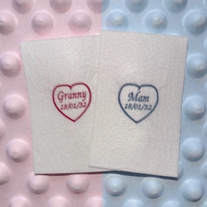 May include: Two white fabric squares with heart-shaped embroidery. One heart is red with the word "Granny" and the date "18/01/32". The other heart is blue with the word "Mam" and the date "18/01/32".