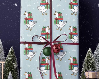 May include: A wrapped gift with a light blue background featuring a pattern of geese carrying stacks of presents and snowflakes. The gift is tied with a burgundy ribbon and ornaments. Miniature Christmas trees and a toy car with a gift on top are in the foreground.