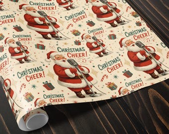 May include: Wrapping paper with a repeating pattern of Santa Claus singing into a microphone, with the words "Christmas Cheer!" and festive illustrations. The paper is rolled up on a dark wooden surface.