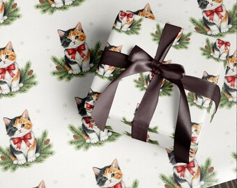May include: White wrapping paper with a repeating pattern of calico kittens wearing red bows, sitting on pine branches. A wrapped gift with a brown satin bow is in the center. The overall theme is festive and cat-themed.