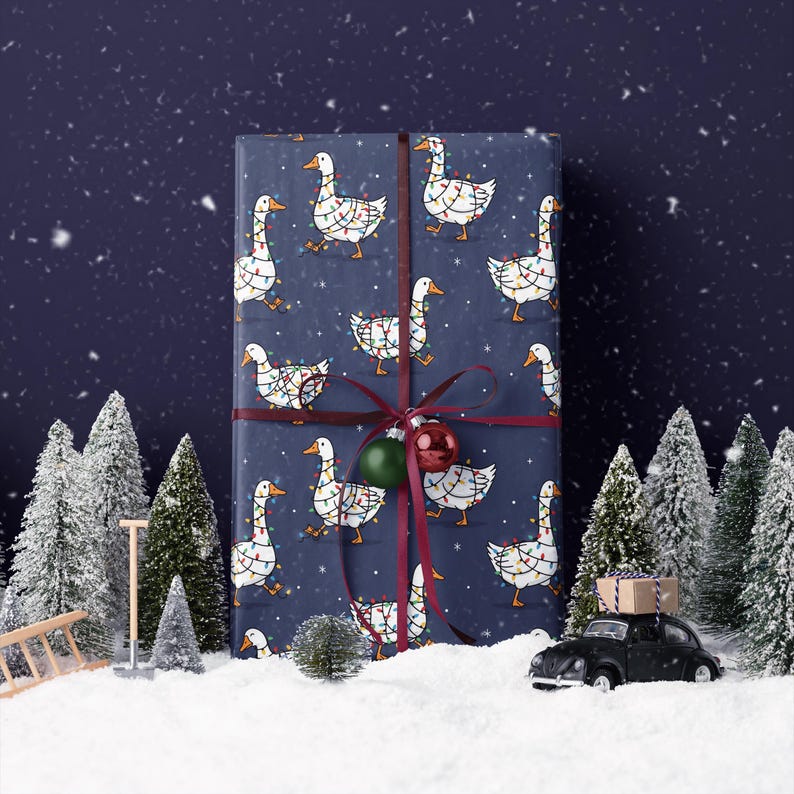 May include: A wrapped gift with navy blue wrapping paper featuring white geese decorated with Christmas lights. The gift is tied with a burgundy ribbon and adorned with a green and red ornament. The scene is set in a snowy winter landscape.