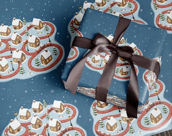 May include: Blue wrapping paper with a repeating pattern of a winter village scene. The design features snow-covered houses, red roads, and evergreen trees. A wrapped gift with a brown satin ribbon is in the foreground.