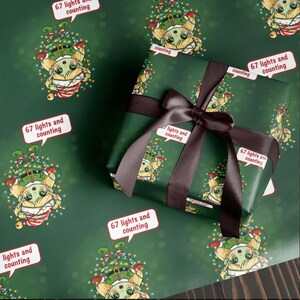 May include: Dark green wrapping paper featuring a cartoon character in a Christmas tree hat and the text "67 lights and counting." A wrapped gift with a brown ribbon and bow is visible.