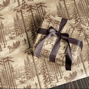 May include: A wrapped gift box tied with a dark brown satin ribbon. The wrapping paper displays a sepia-toned winter scene with skiers, horse-drawn sleighs, and cabins amongst tall pine trees. The theme is a vintage winter holiday.