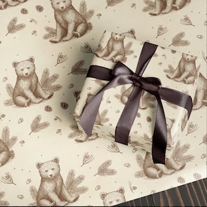 May include: Gift wrap featuring a repeating pattern of brown bears, pine needles, and pine cones on a cream background. A wrapped gift with a dark brown satin ribbon and bow is in the foreground. The gift wrap is perfect for nature lovers.