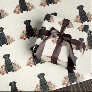 May include: Wrapping paper featuring a repeating pattern of black Labrador Retrievers, gifts, and pinecones on a cream background. A wrapped gift with a brown satin ribbon and bow is in the foreground. The overall theme is festive and dog-themed.