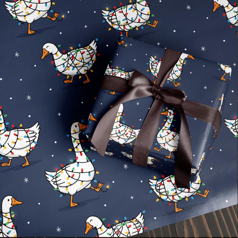 May include: Gift wrap featuring a repeating pattern of white geese adorned with colorful Christmas lights on a navy blue background. A wrapped gift with a brown satin ribbon is in the image. White snowflakes and stars are scattered across the background.