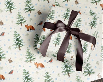 May include: Gift wrapped in winter-themed paper with a brown satin ribbon. The paper features illustrations of foxes, rabbits, birds, snow-covered pine trees, and snowflakes on a cream background. The ribbon is tied in a bow.