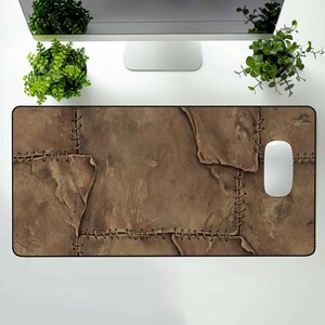 Könnte beinhalten: Ein rechteckiges braunes Mauspad mit einem genähten Lederdesign. Das Pad hat ein strukturiertes Aussehen mit sichtbaren Nahtdetails, und eine weiße Computermaus liegt auf der rechten Seite. Die Gesamtästhetik ist rustikal und vintage.