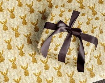 May include: A wrapped gift with a brown satin ribbon and bow. The gift wrap features a repeating pattern of gold angel figures on a cream-colored background with script. The gift is on a matching wrapping paper.