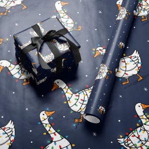 May include: Gift wrap featuring a navy blue background with white geese decorated with colorful Christmas lights. A wrapped gift with a black ribbon and a roll of matching wrapping paper are displayed.