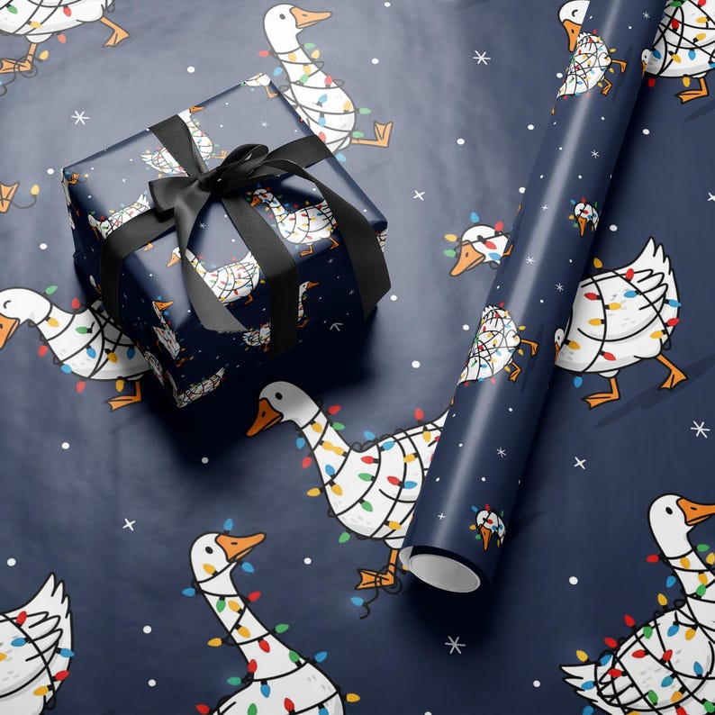 May include: Gift wrap featuring a navy blue background with white geese decorated with colorful Christmas lights. A wrapped gift with a black ribbon and a roll of matching wrapping paper are displayed.
