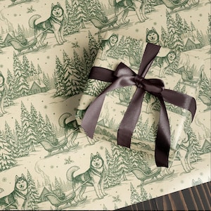 Op de afbeelding: Cadeau verpakt in papier met een herhaald patroon van groene husky's die sleeën door een besneeuwd landschap trekken. Het cadeau is vastgebonden met een donkerbruin satijnen lint. De achtergrond is lichtbeige.