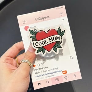 May include: A red heart-shaped sticker with the words "COOL MOM" on a banner, surrounded by green leaves. The sticker is on a white card designed to look like an Instagram post.