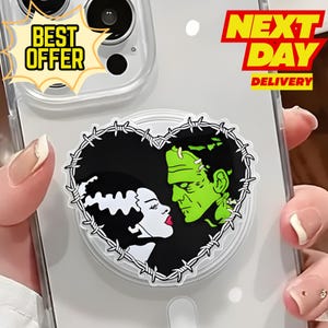 May include: A clear phone case with a heart-shaped pop socket featuring a black and white Bride of Frankenstein and a green Frankenstein's monster design. The pop socket is surrounded by barbed wire. The case has "BEST OFFER" and "NEXT DAY DELIVERY" text.