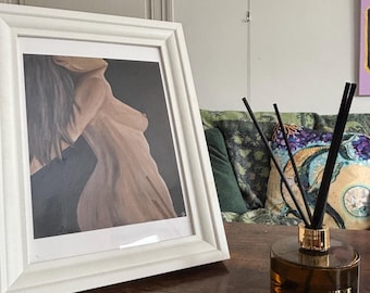 Può includere: Un'opera d'arte incorniciata raffigurante una figura nuda in tonalità beige e marrone, su sfondo scuro. Un diffusore in vetro marrone con bastoncini neri e un collare dorato è posto su una superficie di legno. La parola "VIEVE" è stampata sul diffusore.