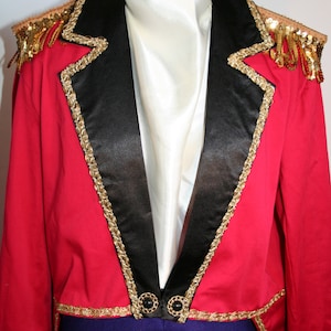 May include: A red and black tailcoat with gold trim and a white shirt. The tailcoat has a high collar and a long tail. The shirt is tucked into the tailcoat and has a white collar.