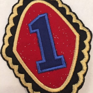 May include: A red felt patch with a gold and black border. The patch has a large blue number one in the center.