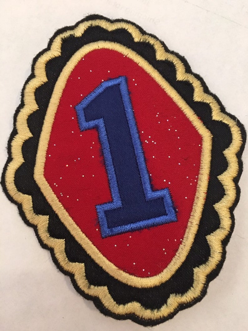 May include: A red felt patch with a gold and black border. The patch has a large blue number one in the center.