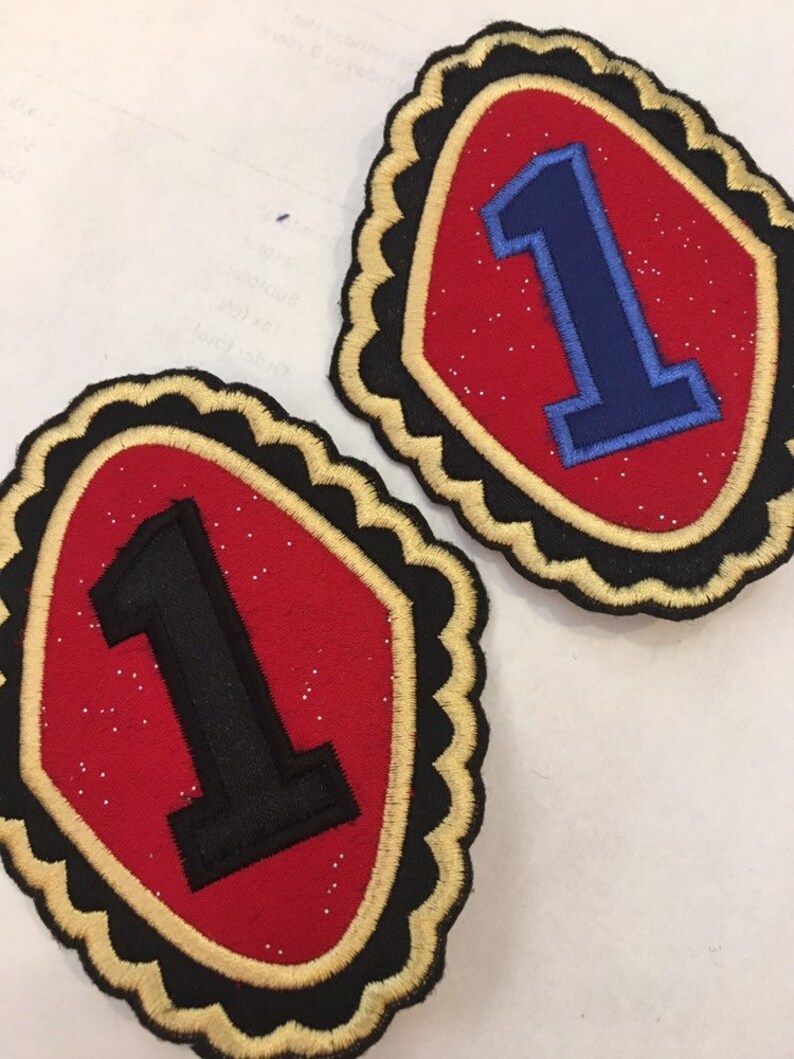 May include: Two red felt patches with gold trim and black or blue felt number ones. The patches have a scalloped edge.