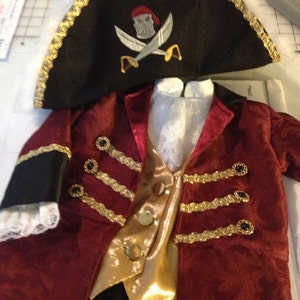 May include: A red velvet pirate costume with gold trim and a black pirate hat with a skull and crossbones design.
