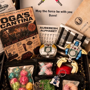 May include: A themed gift box with Star Wars merchandise. Includes a "May the force be with you" card, Oga's Cantina poster, Aurebesh alphabet sheet, popcorn, candy, a keychain, and other collectibles.