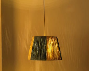 May include: A hanging pendant light with a trapezoidal shade. The shade is divided into two sections, one dark green and the other gold. The light fixture is suspended from a thin cord attached to a circular ceiling mount.