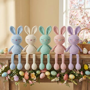 Könnte beinhalten: Fünf Häschen-Puppen in Pastellfarben: Hellblau, Creme, Mintgrün, Rosa und Lavendel. Jedes Häschen hat geschlossene Augen und lange, herabhängende Beine. Sie sind auf einer Holzoberfläche mit Osterdekorationen angeordnet.