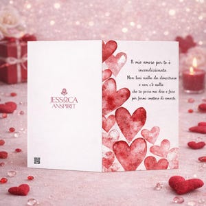 May include: A greeting card featuring a watercolor design of red hearts. The card has text in Italian. The Jessica Anspirit logo is visible. The background is pink with scattered hearts and decorative elements.