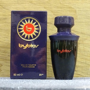 Puede incluir: Un juego de botella y caja de perfume azul oscuro. La caja presenta el nombre de la marca "byblos" en letras doradas, junto con un dise&ntilde;o de sol. La botella es negra con una tapa azul oscuro y el nombre de la marca en rojo.