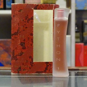 Puede incluir: Un conjunto de perfume con frasco y caja. El frasco tiene forma curva con la palabra "PYTHON" impresa verticalmente. La caja es roja con un estampado de piel de serpiente y la palabra "PYTHON" impresa verticalmente.