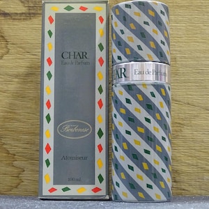 May include: A perfume bottle and box set. The cylindrical bottle and box are decorated with a repeating pattern of gray, yellow, and white diamonds. The box is gray with the word "CHAR" and "Eau de Parfum" printed on it. The box also has a decorative border.