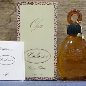 May include: A vintage perfume bottle with a brown glass body and a matching stopper. The bottle is accompanied by a box and a small card, both featuring the brand name "Borbonese" and the fragrance name "Gia". The box has a beige background with a brown border.