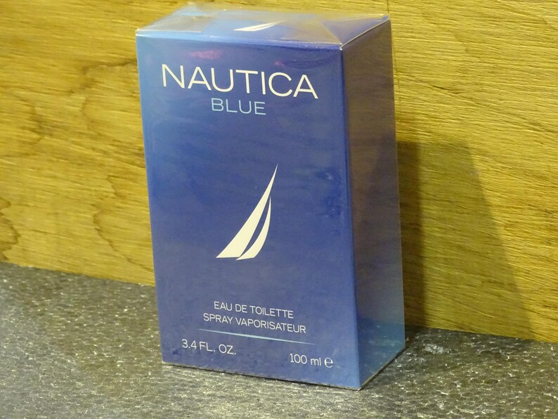 May include: A blue rectangular box of Nautica Blue eau de toilette. The box features the brand name in white, a white sailboat logo, and the text "EAU DE TOILETTE SPRAY VAPORISATEUR". It contains 3.4 fl. oz. / 100 ml.