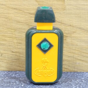 May include: A vintage perfume bottle with a rectangular yellow body and a dark green cap. The bottle features a green gem in a diamond shape and the word "Lombarde" in a curved font.
