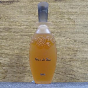Może przedstawiać: Butelka perfum z matowym, pomarańczowym szklanym korpusem i ciemnoszarą nakrętką. Butelka ma kwiatowy wzór u góry, a z przodu nadrukowano napis "Fleur de Boa". Nazwa marki "boa" jest wydrukowana na dole.