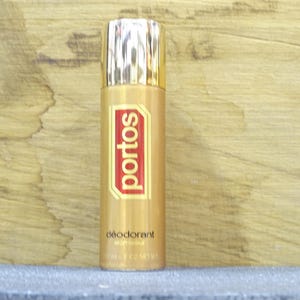 Op de afbeelding: Een goudkleurige deodorant sprayfles met een gouden dop en een rood en goud label met de tekst "portos". De onderkant van het label luidt "déodorant". De fles is 7 oz netto.