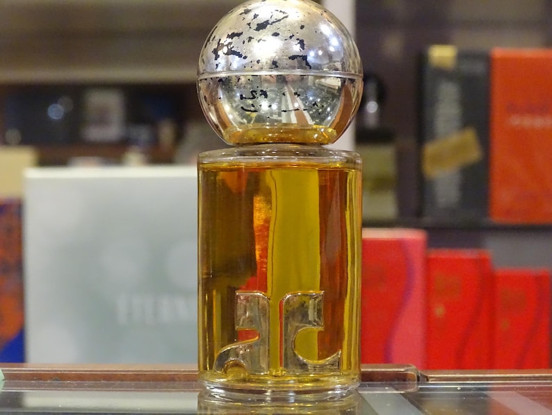 May include: A perfume bottle with a silver and gold spherical cap. The clear glass bottle contains a golden liquid and features a gold emblem. The background includes other perfume boxes.