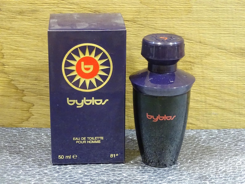 Puede incluir: Un juego de botella y caja de perfume azul oscuro. La caja presenta un logotipo de sol con el nombre de la marca "byblos". La botella es azul oscuro con una tapa a juego. El texto "EAU DE TOILETTE POUR HOMME" est&aacute; impreso en la caja.