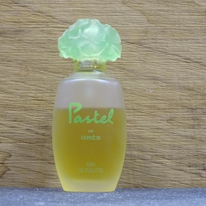 Op de afbeelding: Een vintage parfumflesje van "Pastel de Grès" eau de toilette. De fles is lichtgeel van kleur met een matglaseffect. De dop is lichtgroen, in de vorm van een bloem. De woorden "Pastel de Grès" zijn in groene letters geschreven.
