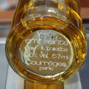 May include: A clear glass bottle of eau de toilette with a golden liquid inside. The label reads "emprunte eau de toilette 90% vol 57ml Courr&egrave;ges paris."