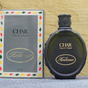 May include: A black oval-shaped bottle of "CHAR Eau de Cologne" with a matching box. The box and bottle feature the name "Borbonese" in a gold script. The box has a gray background with a colorful border.