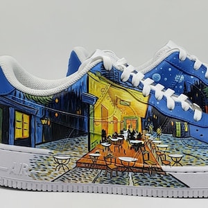 May include: Pair of custom-painted sneakers featuring a vibrant depiction of Van Gogh's "Cafe Terrace at Night." The shoes have a blue and white color scheme, with the artwork wrapping around the sides and toe. The soles are white.