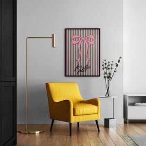 May include: A rectangular wall art print in a black frame featuring a pink bow centred over vertical green and pink stripes. The text "for the plot" is printed in black cursive script below the bow. The artwork is displayed on a light grey wall.